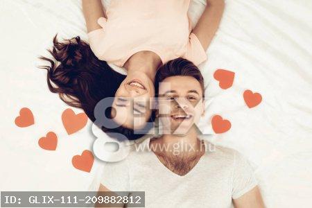 Happy Couple Are Lying In Bed At Valentine's Day. Love Each Other. Sweetheart's Holiday Concept. Origami Roses. Celebrating Date. Young And Handsome. Eyes Closed Couple. Happy Together.