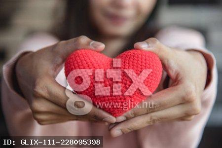 Big red yarn heart holding and giving to front by woman hand. Love and affection in Valentines day concept. Romantic object and health care.