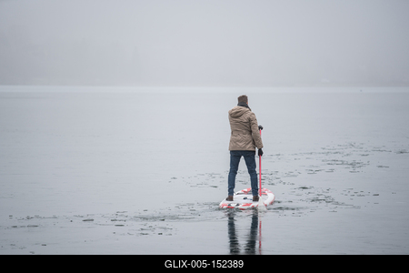 Man standing on stand up paddleboard on icy lake-stock-foto