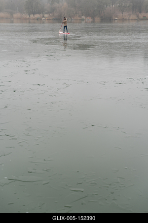 Man standing on stand up paddleboard on icy lake-stock-foto