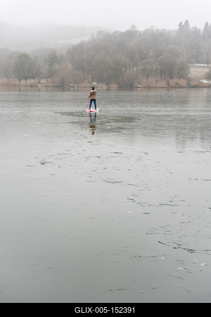 Man standing on stand up paddleboard on icy lake-stock-foto