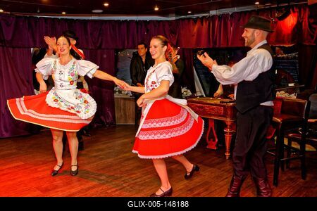 Magyar folklor, népi tánc együttes, két lány táncol magyar öltözékben, férfi tapsol nekik-stock-foto