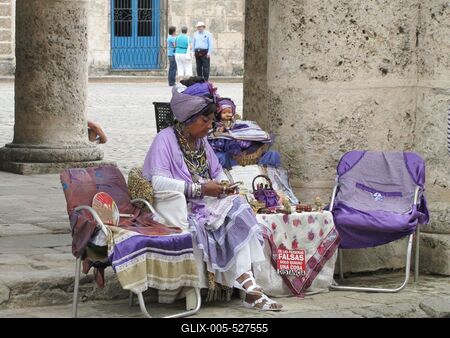 Havana, 25 January 2015Cuban woman in purple selling trinkets. Csecsebecs?it ?rus?t? kubai asszony lila d?szruh?ban a Katedr?lis t?r ?rk?dja alatt. T?bl?j?n spnyol felirat: ker?ljenek a hamisak!-stock-foto