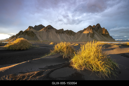 The view of the mountains of Vestrahorn from black volcanic sand beach with grasses at sunset, Stokksnes, South Iceland,-stock-foto