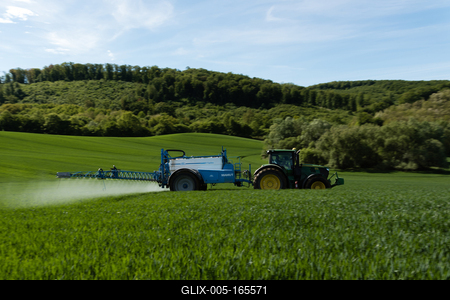 A farmer spraying on the spring wheat field with a John Deere tractor and a mamut topline sprayer. Panning shot.-stock-foto
