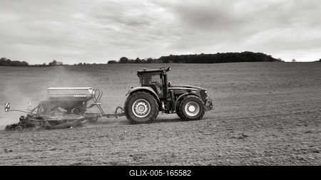 A farmer sowing with a John Deere tractor and a Horsch Pronto 4dc seeding machine. It's a panning shot, that cause the blurry background. Black and white.-stock-foto