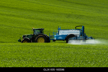 A farmer spraying on the spring wheat field with a John Deere tractor and a mamut topline sprayer. Panning shot.-stock-foto
