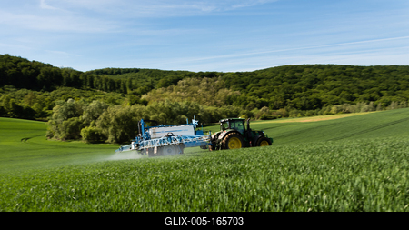 A farmer spraying on the spring wheat field with a John Deere tractor and a mamut topline sprayer. Panning shot.-stock-foto