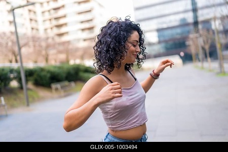 Curly haired hispanic woman joyfully dancing in an urban setting, embracing the sunny day with vibrant energy and carefree movement-stock-foto