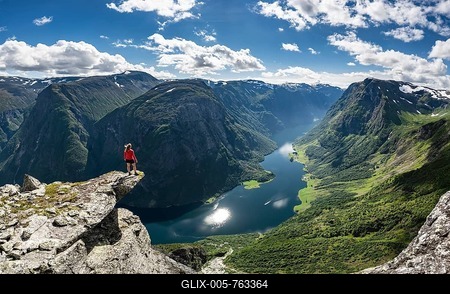 Hiker standing on rocky outcrop, view from the top of Breiskrednosi, mountains and fjord, Nćrřyfjord, Aurland, Norway-stock-foto