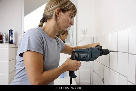 Young woman drilling a hole in a tiled bathroom wall-stock-foto