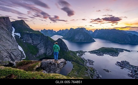 Evening atmosphere, young hiker standing on a rocky outcrop and enjoying the view from Reinebringen, Reinebriggen, Hamnoy, Reine and the Reinefjord with mountains, Moskenes, Moskenesöy, Lofoten, Norway-stock-foto