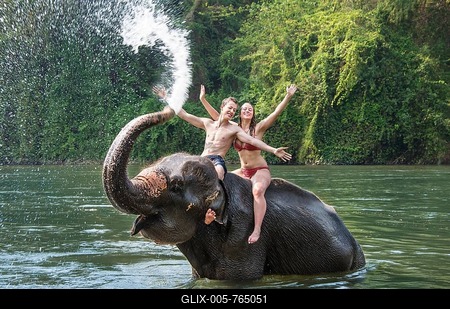 Two teenagers sitting on an Asian Elephant (Elephas maximus), being sprayed with water from the trunk, Kanchanaburi, Thailand-stock-foto