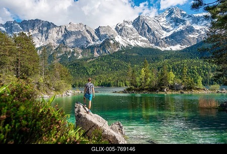 Young man standing on a rock, view into the distance, Eibsee lake and Zugspitze in spring with snow, Wetterstein Mountains, near Grainau, Upper Bavaria, Bavaria, Germany-stock-foto
