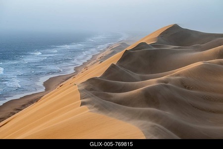 Sand dunes and sea in the evening light, wind blows sand over the dunes, view of the Atlantic coast from high sand dunes, Sandwich Harbour, Namib Naukluft Park, Namibia-stock-foto