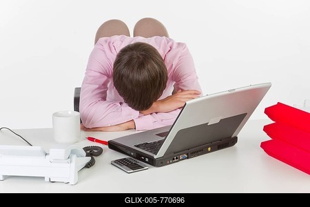 Young man at his desk in the office with a laptop computer, head resting on the desk-stock-foto