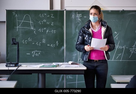 Teacher with winter jacket and face mask in classroom teaching, gestures, corona crisis, Stuttgart, Baden-Württemberg, Germany-stock-foto