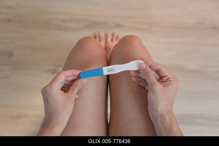 A person holds a positive pregnancy test above their knees, symbolic image of new life, wooden floor-stock-foto
