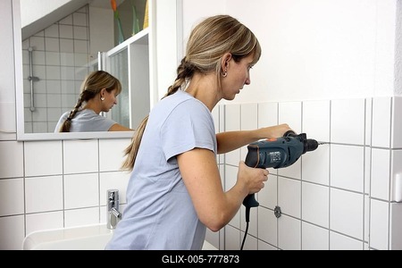 Young woman drilling a hole in a tiled bathroom wall-stock-foto