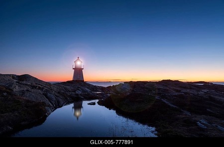 Lighthouse surrounded by rocks at night, lighthouse with lights on at sunset-stock-foto