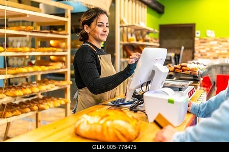 Friendly young latin saleswoman preparing the checkout for a client in an artisan bakery-stock-foto