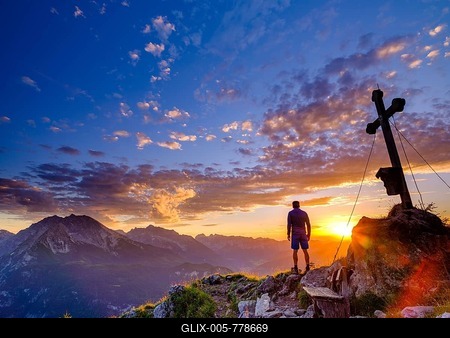 Mountaineer standing at sunset at the summit cross of the Brettgabel, in the background Watzmann, Hochkalter and Reiteralpe, Berchtesgaden Alps, Berchtesgaden National Park, Schönau am Königssee, Berchtesgadener Land, Bavaria, Germany-stock-foto