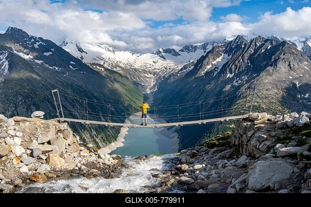 Mountaineers on a suspension bridge over a mountain stream Alelebach, picturesque mountain landscape near the Olpererhütte, view of turquoise-blue lake Schlegeisspeicher, glaciated rocky mountain peaks Hoher Weißzint and Hochfeiler with glacier Schlegeiskees, Berliner Höhenweg, Zillertal Alps, Tyrol, Austria-stock-foto