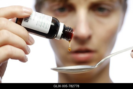 Young woman dripping liquid medicine onto a spoon, against a cold or cough, stomach drops-stock-foto
