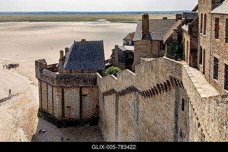 Historic castle wall with a view of a wide expanse of sand and distant buildings under a clear sky, Mont Saint Michel in Normandy, France-stock-foto
