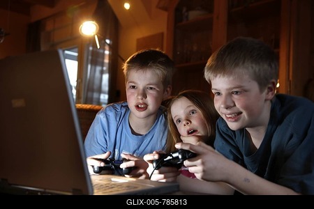 Siblings, 7, 11, 13 years old, with laptop computer in the living room, playing a car racing computer game-stock-foto