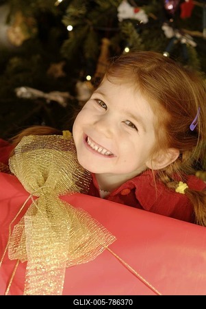 Girl with a big present in front of a Christmas tree on Christmas Eve-stock-foto