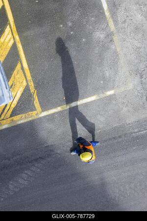 A construction worker in a hard hat walks over tarmac. He casts a long shadow. Stuttgart, Baden-Württemberg, Germany-stock-foto