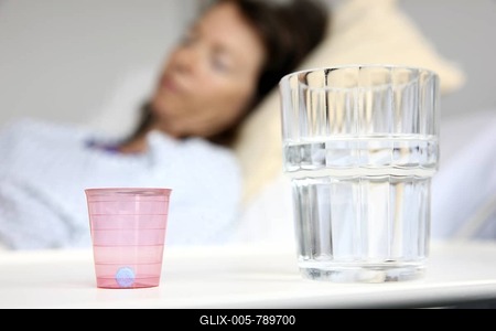 Patient lying in a hospital bed, medicine and glass with water standing on a bedside table, hospital-stock-foto