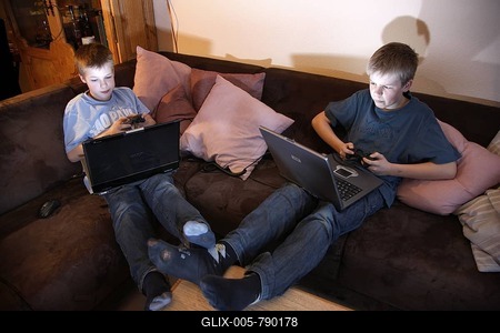 Brothers, 11 and 13 years old, with laptop computer in the living room, playing a car racing computer game on two computers against each other-stock-foto