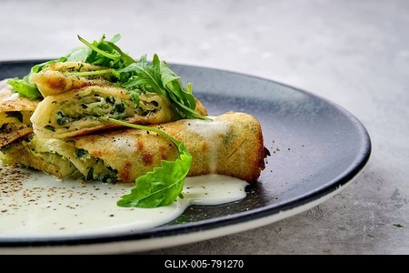 Closeup view of thin crepe stuffed with cheese, arugula and spinach on a plate with creamy sauce-stock-foto