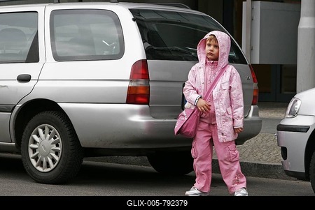 Little girl waits between parking cars to cross the street-stock-foto