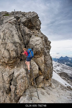 Hiker climbs metal ladder on rock, climber on ridge path with remnants of snow, dramatic cloudy sky, Heilbronner Weg, Allgäu Alps, Allgäu, Bavaria, Germany-stock-foto