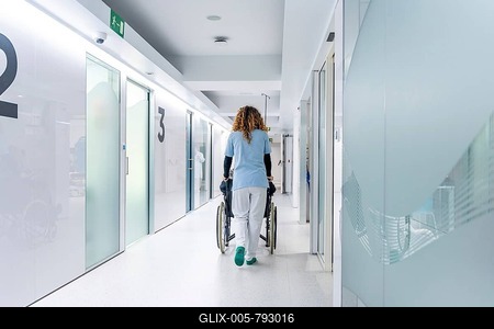 Rear view of nurse pushing a wheelchair along the hospital with a mature woman sitting on it-stock-foto