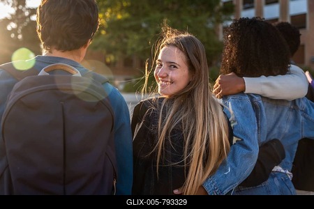 Group of young diverse university students walking arm in arm on campus, one woman turning to camera smiling during golden hour, celebrating friendship and education-stock-foto