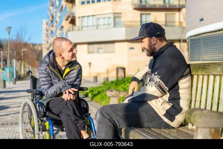 Disabled person in a wheelchair with a friend sitting having fun and talking-stock-foto