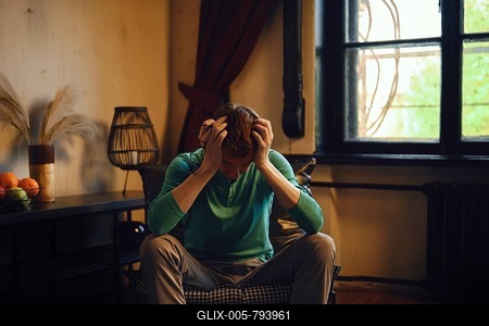 A man sits on a chair visibly overwhelmed and stressed. He put his head in his hands in frustration-stock-foto