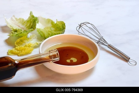 Bowl with cooking oil and aceto balsamico, bottle and whisk, salad leaves-stock-foto