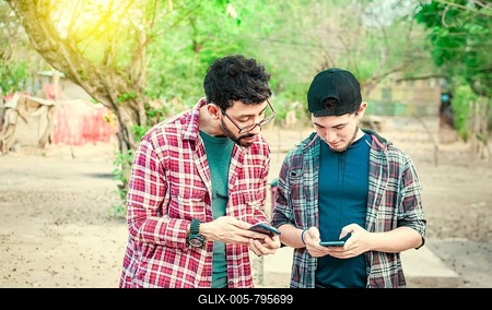 Two teenage guys pointing and checking their cell phones, Two friends looking at the content of their cell phone. Friend showing cell phone to his friend, Smiling friends checking cell phones-stock-foto