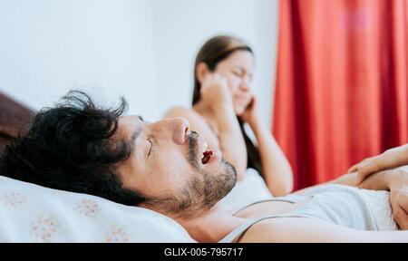 Snoring man in bedroom and wife covering her ears. Husband snoring while the wife suffers and covers her ears. Sleep apnea concept-stock-foto