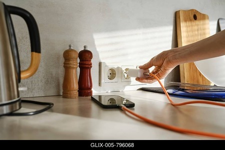A person plugs a smartphone charger into an outlet while standing in a stylish kitchen-stock-foto
