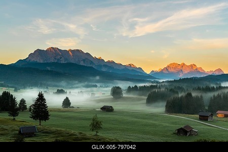 Mountain meadows with small huts in light ground fog and Zugspitz massif in the background at sunrise, Krün, Bavaria, Germany-stock-foto