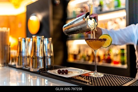Hand of a waiter pouring cocktail into martini glass garnished with lemon in the counter of a luxury night club-stock-foto