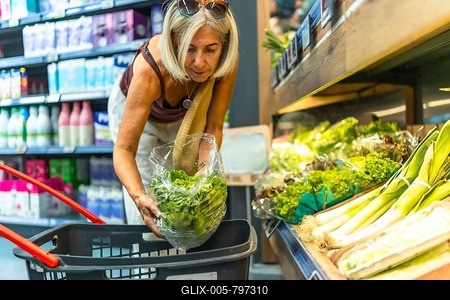 Senior woman picking fresh lettuce in the produce section of a grocery store, putting vegetables in her shopping basket-stock-foto