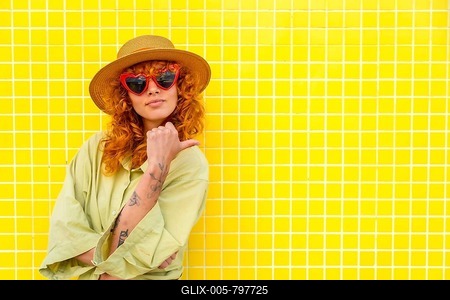 Fashionable influencer posing confidently against a vibrant yellow tiled wall, pointing with her thumb while showcasing her stylish look-stock-foto