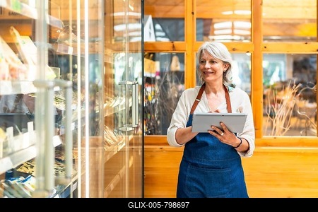 Senior saleswoman wearing apron using digital tablet checking stock availability, working in supermarket-stock-foto